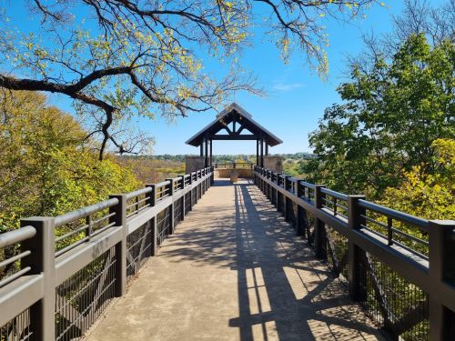 A scenic walkway leads to a gazebo, surrounded by trees and a clear blue sky.
