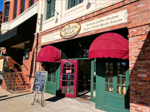 Exterior of Artistic Bean café with red awnings, brick walls, and a chalkboard menu outside.