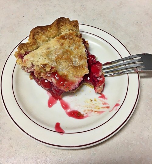 A slice of cherry pie on a plate, with a fork resting beside it and cherry filling oozing out.