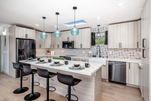 Modern kitchen with light wood cabinets, patterned backsplash, and a large island with bar stools and teal pendant lights.