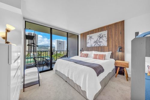 Bright, modern bedroom with a large bed, balcony view, and stylish decor featuring wood accents and city skyline.