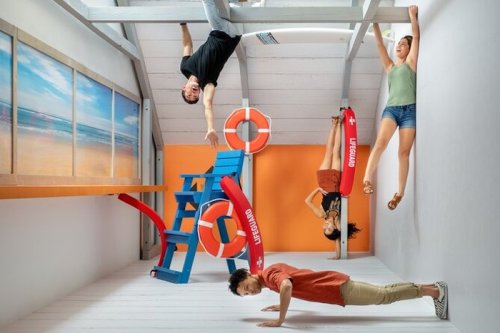 Four people are playfully posed in an upside-down room, with beach-themed decor and lifebuoys.