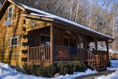 A cozy log cabin with a porch, surrounded by snow and trees, creating a serene winter scene.