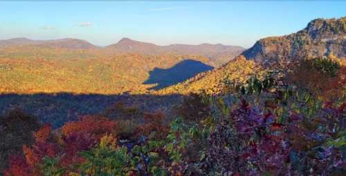 A panoramic view of colorful autumn foliage covering rolling hills under a clear blue sky.