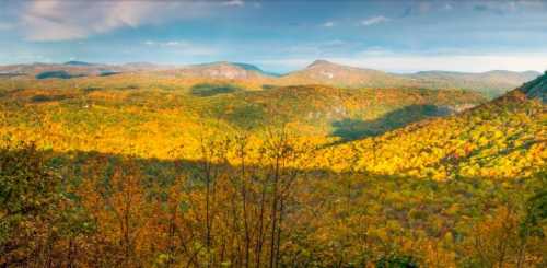 A panoramic view of vibrant autumn foliage covering rolling hills under a partly cloudy sky.