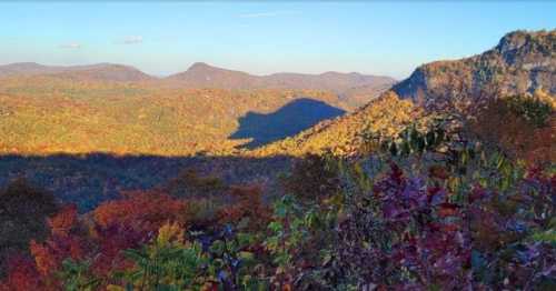 A scenic view of colorful autumn foliage covering rolling hills under a clear blue sky.