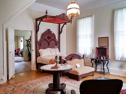 A vintage bedroom featuring a four-poster bed, a small table, and elegant furnishings with soft lighting.