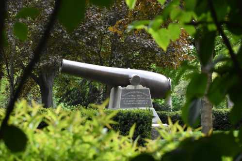 A large cannon monument surrounded by greenery in a park setting.