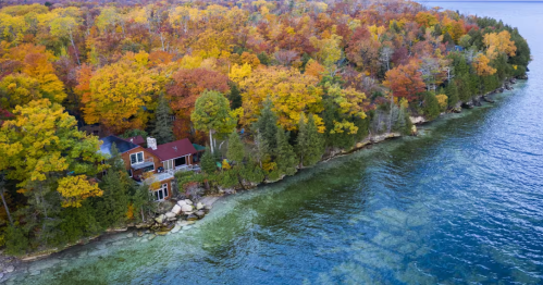Aerial view of a lakefront cabin surrounded by vibrant autumn trees on the rocky Wisconsin shoreline.