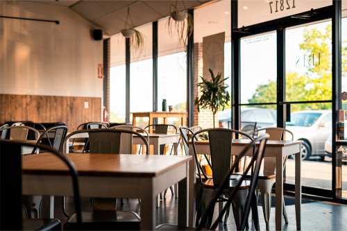 A cozy café interior with wooden tables, metal chairs, and large windows letting in natural light.