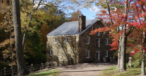 A stone house surrounded by colorful autumn trees and a gravel path, set in a serene natural landscape.