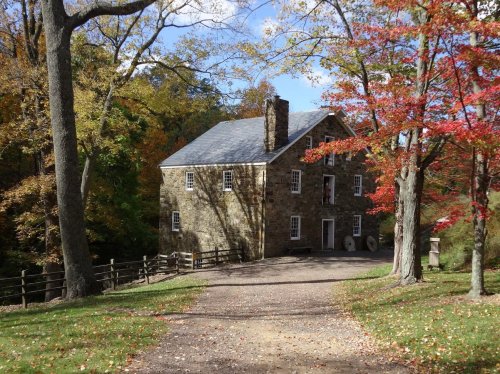A stone house surrounded by colorful autumn trees and a gravel path leading to it.