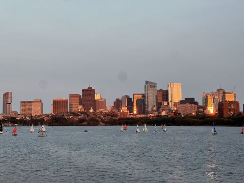 City skyline at sunset with sailboats on the water in the foreground.