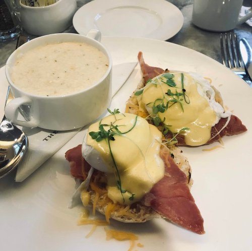 A plate featuring eggs Benedict with ham and hollandaise sauce, alongside a cup of creamy soup.
