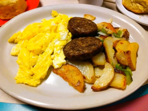 A plate of scrambled eggs, two sausage patties, and seasoned potato chunks with peppers and onions.