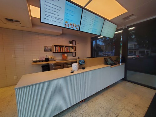 A modern cafe counter with digital menus, a clean design, and a bright, open space.