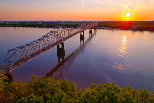 Aerial view of a bridge over a river at sunset, with vibrant colors reflecting on the water.