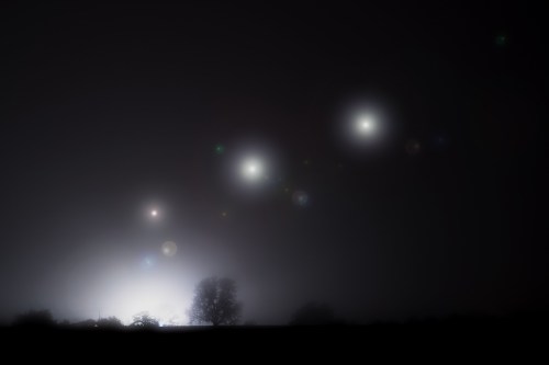 A foggy night scene with glowing orbs in the sky and silhouettes of trees in the foreground.