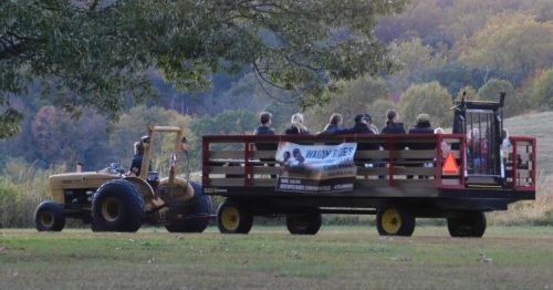 A tractor pulls a wagon filled with people through a scenic landscape during sunset.
