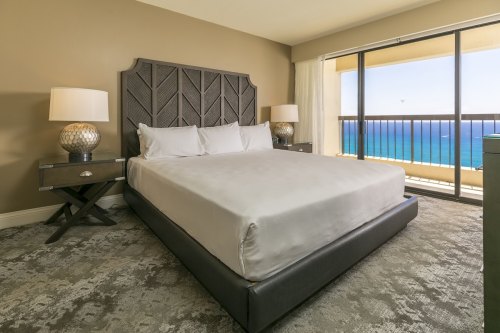 A modern hotel room featuring a king-sized bed, nightstands, and a large window with an ocean view.