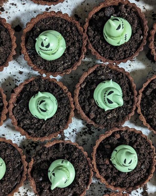 Chocolate tartlets topped with green ghost-shaped decorations on a bed of crushed cookies. Perfect for Halloween!