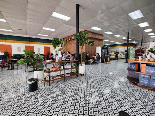 A spacious café interior with patterned tile flooring, plants, and customers seated at tables.