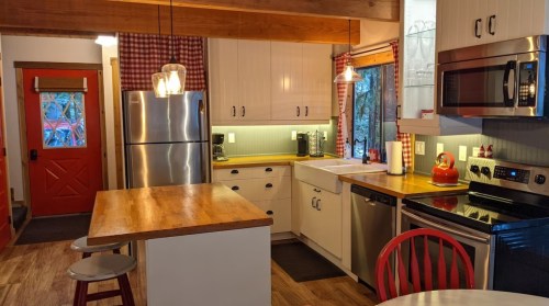 A cozy kitchen with a red door, stainless steel appliances, wooden countertops, and a small dining table.
