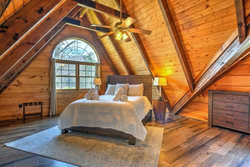 Cozy attic bedroom with wooden beams, a large window, a bed with white linens, and warm lighting.