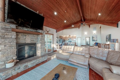 Cozy living room with a stone fireplace, large sectional sofa, and wooden ceiling, leading to an open kitchen area.