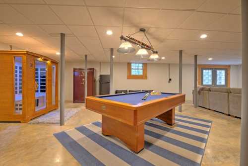 A spacious basement with a pool table, sauna, and cozy seating area, featuring modern lighting and a striped rug.