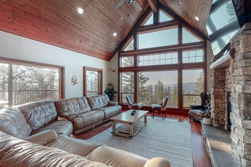 Spacious living room with large windows, wooden ceiling, and cozy furniture, offering mountain views.