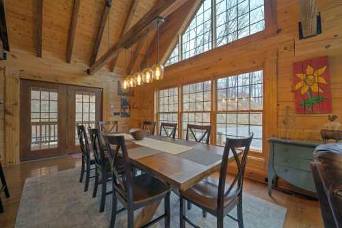 Cozy wooden dining area with a large table, chairs, and large windows overlooking a natural landscape.