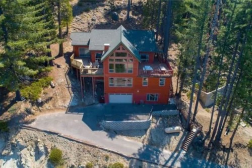 Aerial view of a large red house surrounded by trees on a rocky hillside.