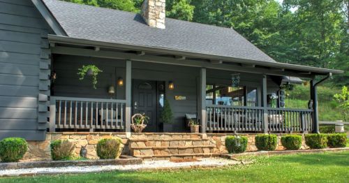 A cozy gray house with a stone porch, surrounded by greenery and a well-maintained lawn.