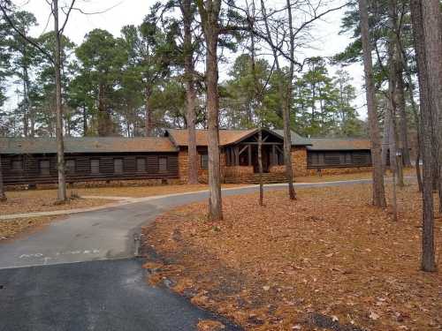 A rustic lodge surrounded by trees, with a gravel path leading to the entrance, set in a wooded area.