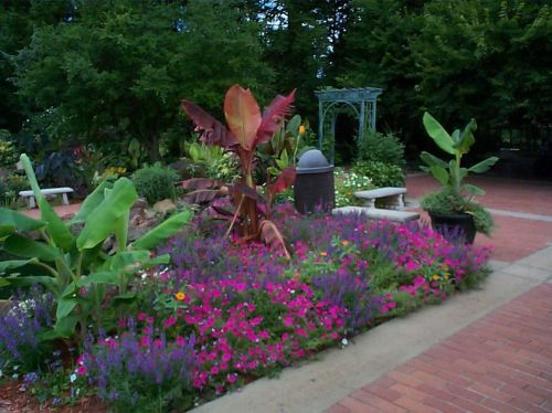 A vibrant garden featuring colorful flowers, lush greenery, and a decorative gazebo in the background.