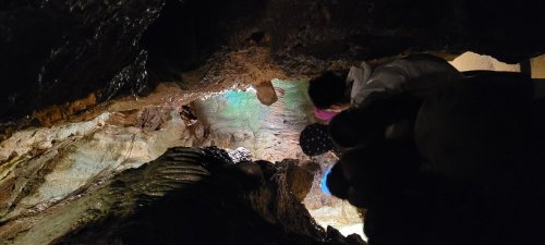A view from above into a cave, showing water and rock formations, with people visible at the edge.