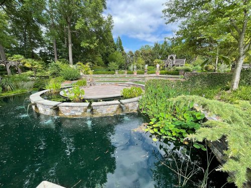 A serene garden scene featuring a circular stone platform surrounded by lush greenery and a tranquil pond.