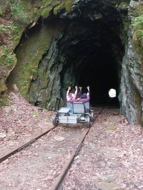Two people on a cart raise their hands while riding on tracks through a dark tunnel surrounded by rocky walls.