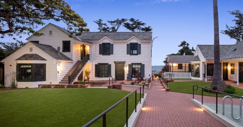 A charming coastal property with white buildings, green lawns, and a pathway leading to the ocean in the background.