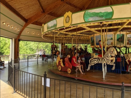 A colorful carousel with children riding various animals, set in a spacious, well-lit pavilion.