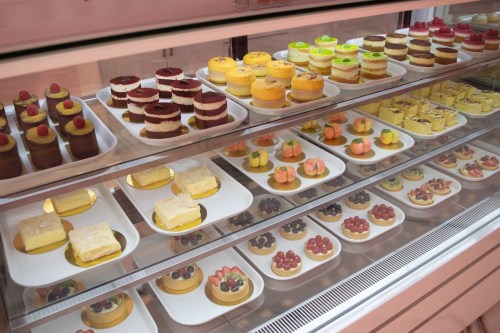 A display case filled with various colorful desserts, including cakes and pastries, arranged on white plates.