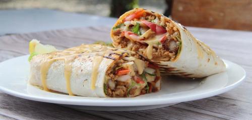 Two grilled burritos filled with meat, vegetables, and cheese, drizzled with sauce, served on a white plate.