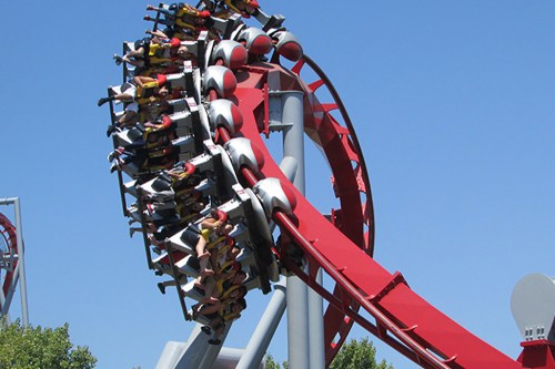 A roller coaster with riders experiencing a thrilling drop against a clear blue sky.