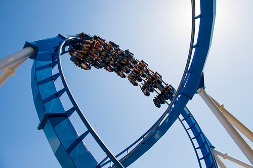 A roller coaster twists through a loop against a clear blue sky, with riders enjoying the thrill.