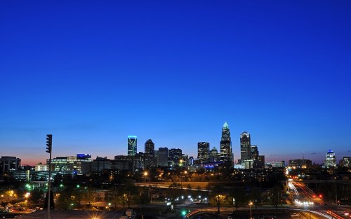 City skyline at dusk, featuring tall buildings and illuminated streets against a deep blue sky.
