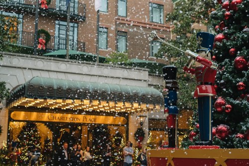 A festive scene with a nutcracker statue, holiday decorations, and snow falling in front of Charleston Place.