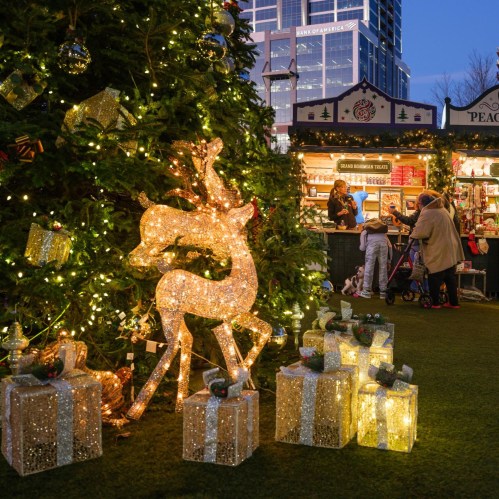 A festive scene with a glowing reindeer, Christmas trees, and people shopping at a holiday market.