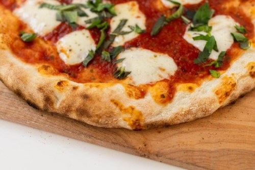 Close-up of a freshly baked pizza with tomato sauce, mozzarella cheese, and fresh basil on a wooden board.
