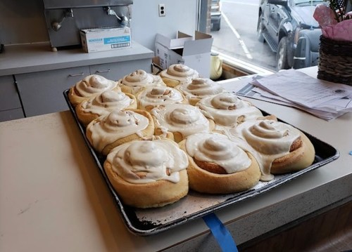 A tray of freshly baked cinnamon rolls with creamy icing, displayed in a cozy bakery setting.